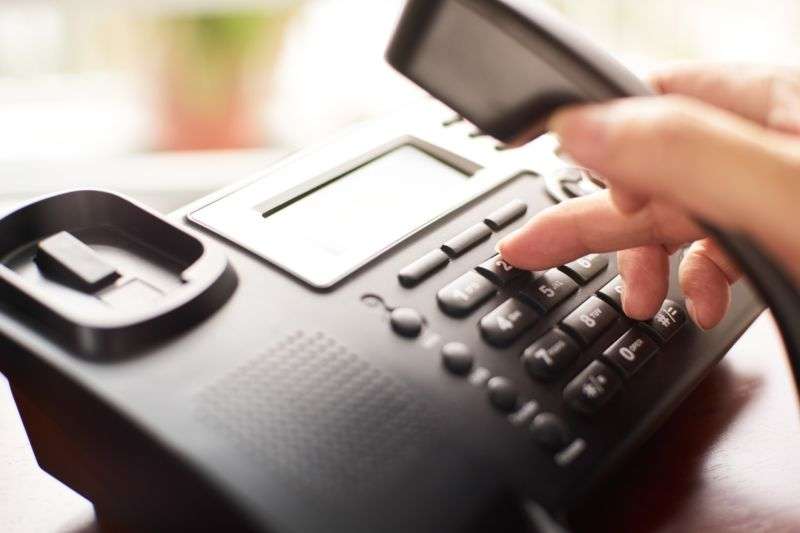 A person's hand dials a landline phone.