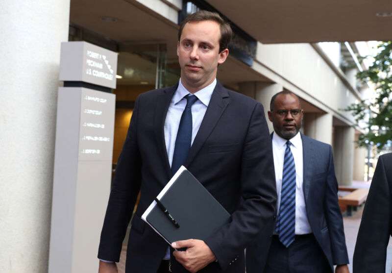 A man in a suit carries a folder while walking.