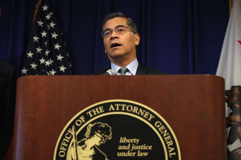 A man in a suit speaks into a microphone at a podium.