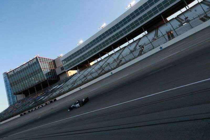 A race car speeds along a track in front of mostly empty stands.