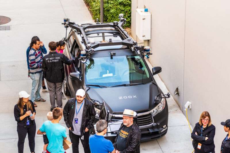 People examine a Zoox test vehicle in 2019. The company has yet to show off the custom-designed vehicle it plans to use for its commercial service.