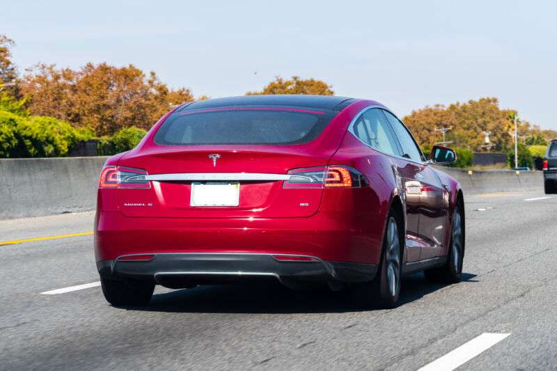 A red sedan cruises down a tree-lined highway.