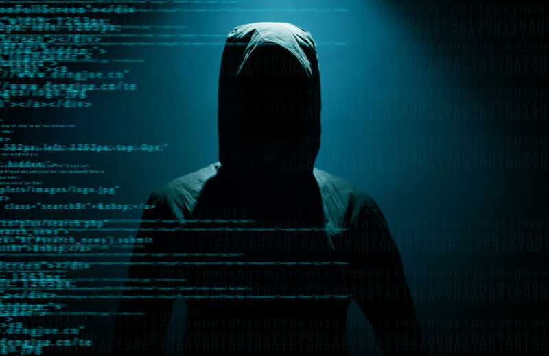 Stock photo of a hooded figure hiding behind computer code.